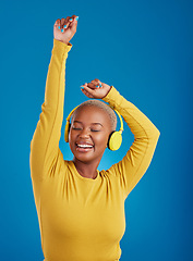 Image showing Black woman with headphones, dance and listen to music with rhythm and fun with freedom on blue background. Happy female with arms raised, streaming radio with dancing and carefree in studio