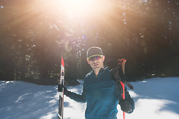 Image showing Portrait handsome male athlete with cross country skis in hands and goggles, training in snowy forest. Healthy winter lifestyle concept.