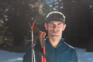 Image showing Portrait handsome male athlete with cross country skis in hands and goggles, training in snowy forest. Healthy winter lifestyle concept.