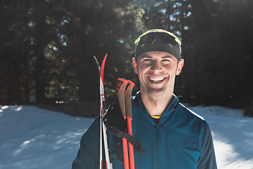 Image showing Portrait handsome male athlete with cross country skis in hands and goggles, training in snowy forest. Healthy winter lifestyle concept.