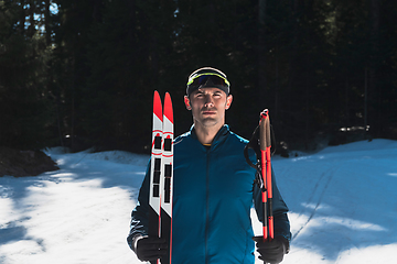 Image showing Portrait handsome male athlete with cross country skis in hands and goggles, training in snowy forest. Healthy winter lifestyle concept.