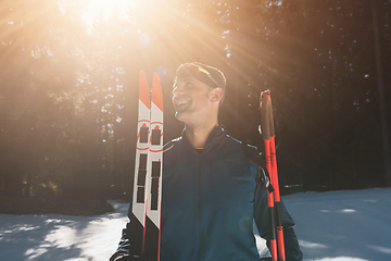 Image showing Portrait handsome male athlete with cross country skis in hands and goggles, training in snowy forest. Healthy winter lifestyle concept.