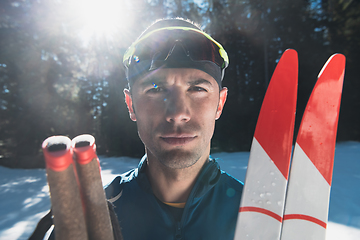 Image showing Portrait handsome male athlete with cross country skis in hands and goggles, training in snowy forest. Healthy winter lifestyle concept.