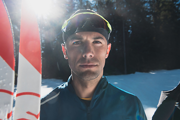 Image showing Portrait handsome male athlete with cross country skis in hands and goggles, training in snowy forest. Healthy winter lifestyle concept.