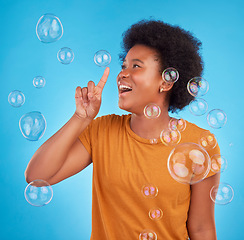 Image showing Happy, bubbles and pop with black woman in studio for light, entertainment and satisfaction. Magic, rainbow and creative with female isolated on blue background for burst, happiness and color