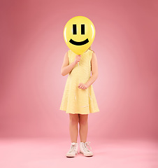 Image showing Smiley face, balloon and child in studio, covering and hiding against a pink background space. Happy, emoji and girl holding toy, game and playing while posing behind inflatable, fun and innocent