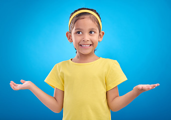 Image showing Girl, child and shrug with happy or unsure face in studio with arms and hands stretched with a smile. Kid on blue background clueless, doubt and confused about question or reaction with hand gesture
