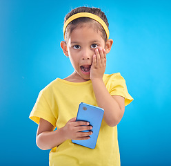 Image showing Phone, shock and portrait of child on blue background with wow, omg and surprise expression in studio. Technology, childhood and face of girl shocked for news, announcement or message on smartphone