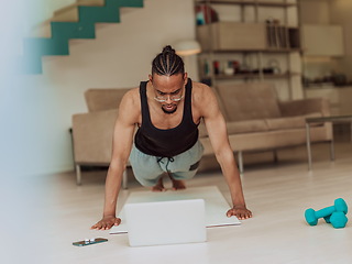 Image showing Young African American man working push-ups in the living room while watching online training on laptop