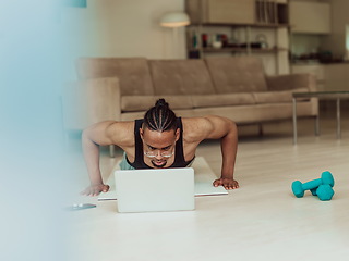 Image showing Young African American man working push-ups in the living room while watching online training on laptop