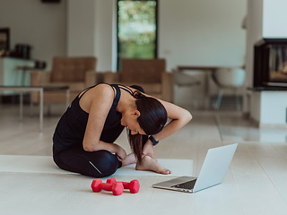 Image showing A young woman in sportswear is sitting in the living room and preparing for online training while using a laptop