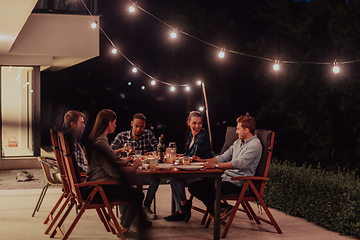 Image showing A group of young diverse people having dinner on the terrace of a modern house in the evening. Fun for friends and family. Celebration of holidays, weddings with barbecue.