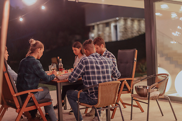 Image showing A group of young diverse people having dinner on the terrace of a modern house in the evening. Fun for friends and family. Celebration of holidays, weddings with barbecue.