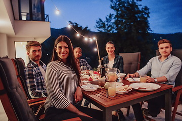 Image showing A group of young diverse people having dinner on the terrace of a modern house in the evening. Fun for friends and family. Celebration of holidays, weddings with barbecue.