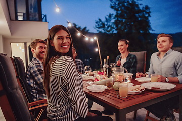 Image showing A group of young diverse people having dinner on the terrace of a modern house in the evening. Fun for friends and family. Celebration of holidays, weddings with barbecue.