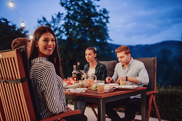 Image showing A group of young diverse people having dinner on the terrace of a modern house in the evening. Fun for friends and family. Celebration of holidays, weddings with barbecue.