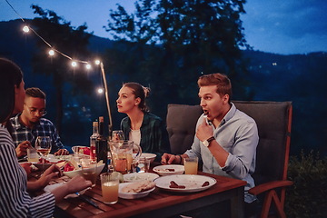 Image showing A group of young diverse people having dinner on the terrace of a modern house in the evening. Fun for friends and family. Celebration of holidays, weddings with barbecue.