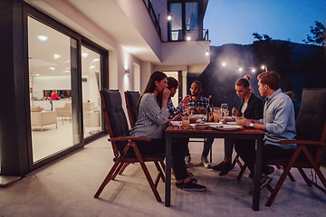 Image showing A group of young diverse people having dinner on the terrace of a modern house in the evening. Fun for friends and family. Celebration of holidays, weddings with barbecue.