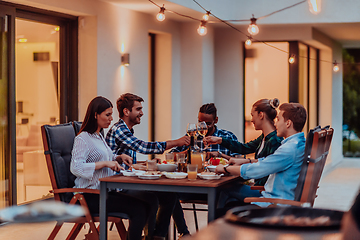 Image showing A group of young diverse people having dinner on the terrace of a modern house in the evening. Fun for friends and family. Celebration of holidays, weddings with barbecue.