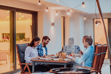 Image showing A group of young diverse people having dinner on the terrace of a modern house in the evening. Fun for friends and family. Celebration of holidays, weddings with barbecue.