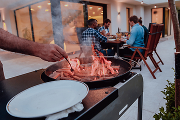 Image showing A group of friends and family barbecue together in the evening on the terrace in front of a large modern house