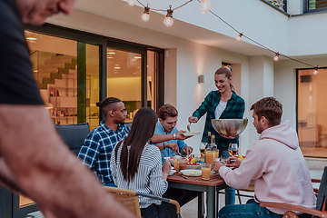 Image showing A group of young diverse people having dinner on the terrace of a modern house in the evening. Fun for friends and family. Celebration of holidays, weddings with barbecue.