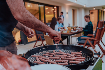 Image showing A group of friends and family barbecue together in the evening on the terrace in front of a large modern house