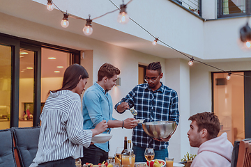 Image showing A group of friends and family barbecue together in the evening on the terrace in front of a large modern house