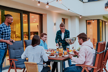 Image showing A group of young diverse people having dinner on the terrace of a modern house in the evening. Fun for friends and family. Celebration of holidays, weddings with barbecue.