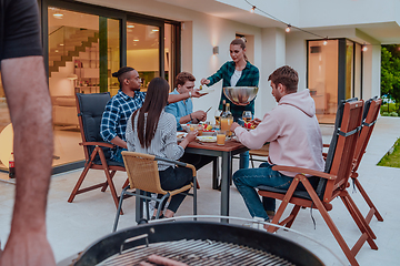 Image showing A group of young diverse people having dinner on the terrace of a modern house in the evening. Fun for friends and family. Celebration of holidays, weddings with barbecue.