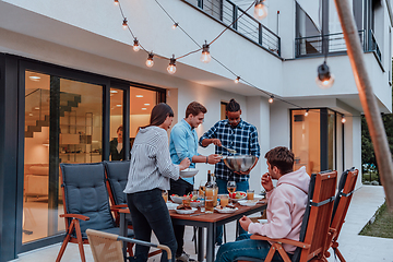 Image showing A group of young diverse people having dinner on the terrace of a modern house in the evening. Fun for friends and family. Celebration of holidays, weddings with barbecue.