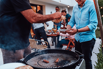 Image showing A group of friends and family barbecue together in the evening on the terrace in front of a large modern house