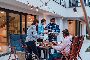 Image showing A group of young diverse people having dinner on the terrace of a modern house in the evening. Fun for friends and family. Celebration of holidays, weddings with barbecue.