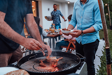 Image showing A group of friends and family barbecue together in the evening on the terrace in front of a large modern house