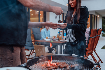 Image showing A group of friends and family barbecue together in the evening on the terrace in front of a large modern house