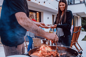 Image showing A group of friends and family barbecue together in the evening on the terrace in front of a large modern house