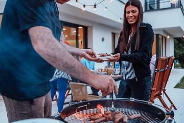 Image showing A group of friends and family barbecue together in the evening on the terrace in front of a large modern house