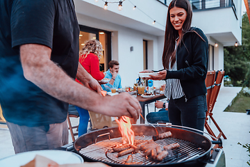 Image showing A group of friends and family barbecue together in the evening on the terrace in front of a large modern house