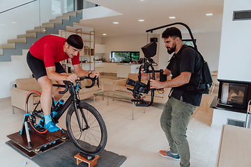 Image showing A cameraman filming an athlete riding a triathlon bike on a simulation machine in a modern living room. Training in pandemic conditions.