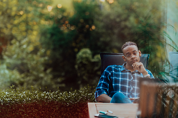 Image showing An African American man sitting in front of the house on a modern terrace and stares thoughtfully at the camera