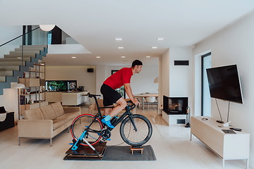 Image showing A man riding a triathlon bike on a machine simulation in a modern living room. Training during pandemic conditions.