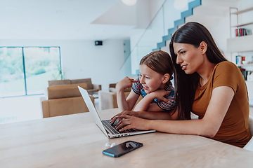 Image showing Mother with her daughter talking on laptop with family and friends while sitting in modern living room of big house