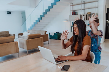 Image showing Mother with her daughter talking on laptop with family and friends while sitting in modern living room of big house