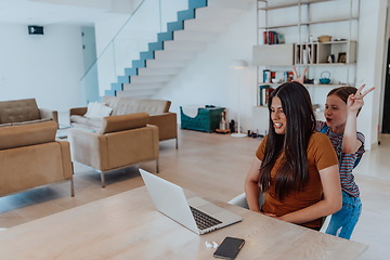 Image showing Mother with her daughter talking on laptop with family and friends while sitting in modern living room of big house