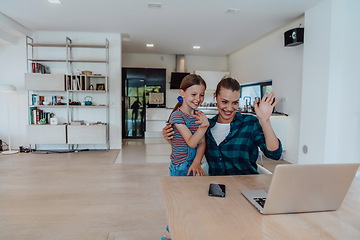 Image showing Mother with her daughter talking on laptop with family and friends while sitting in modern living room of big house