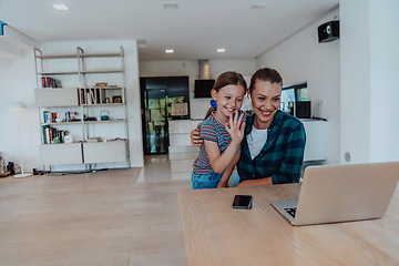 Image showing Mother with her daughter talking on laptop with family and friends while sitting in modern living room of big house