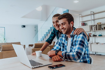 Image showing A young married couple is talking to parents, family and friends on a video call via a laptop while sitting in the living room of their modern house