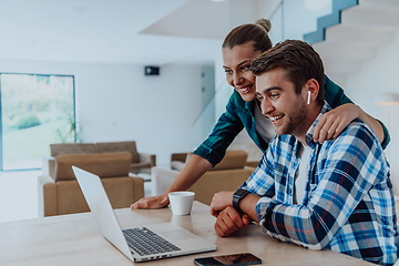 Image showing A young married couple is talking to parents, family and friends on a video call via a laptop while sitting in the living room of their modern house