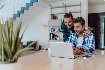 Image showing A young married couple is talking to parents, family and friends on a video call via a laptop while sitting in the living room of their modern house