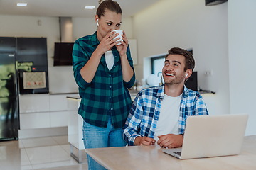 Image showing A young married couple is talking to parents, family and friends on a video call via a laptop while sitting in the living room of their modern house